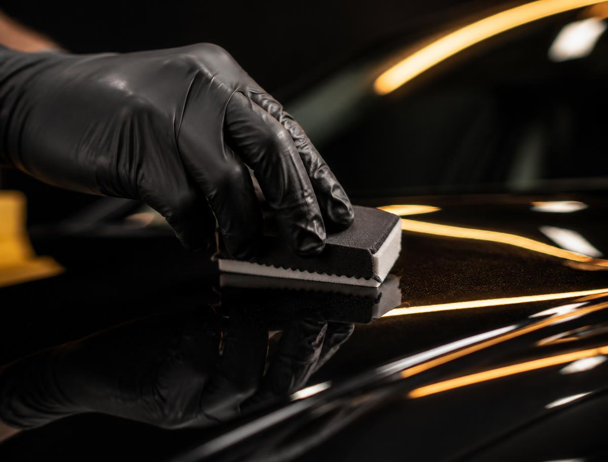 Technician applying ceramic coating to a glossy black car panel